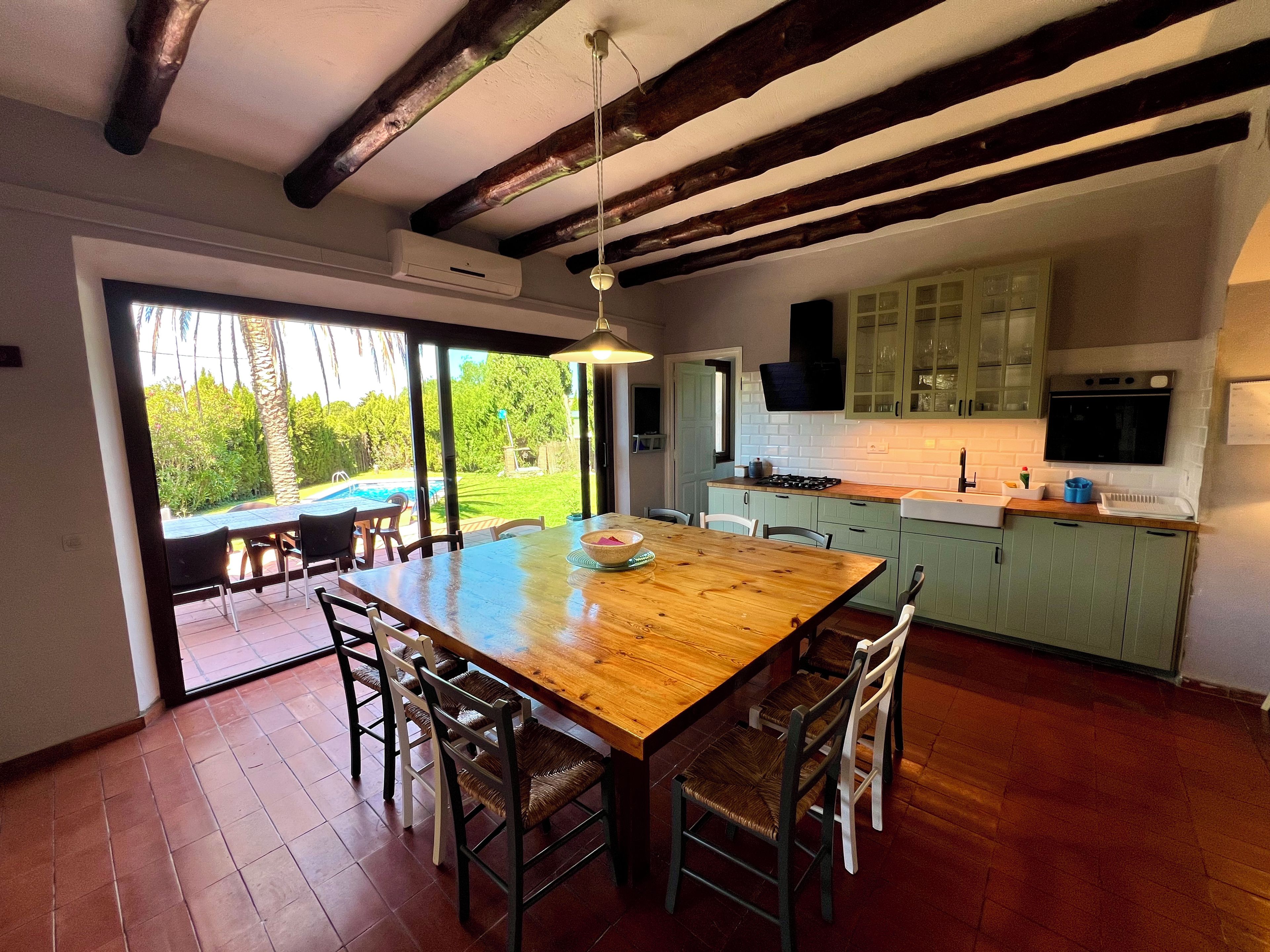 A spacious dining area with a wooden table and chairs, a kitchen with green cabinets, and a view of a swimming pool.
