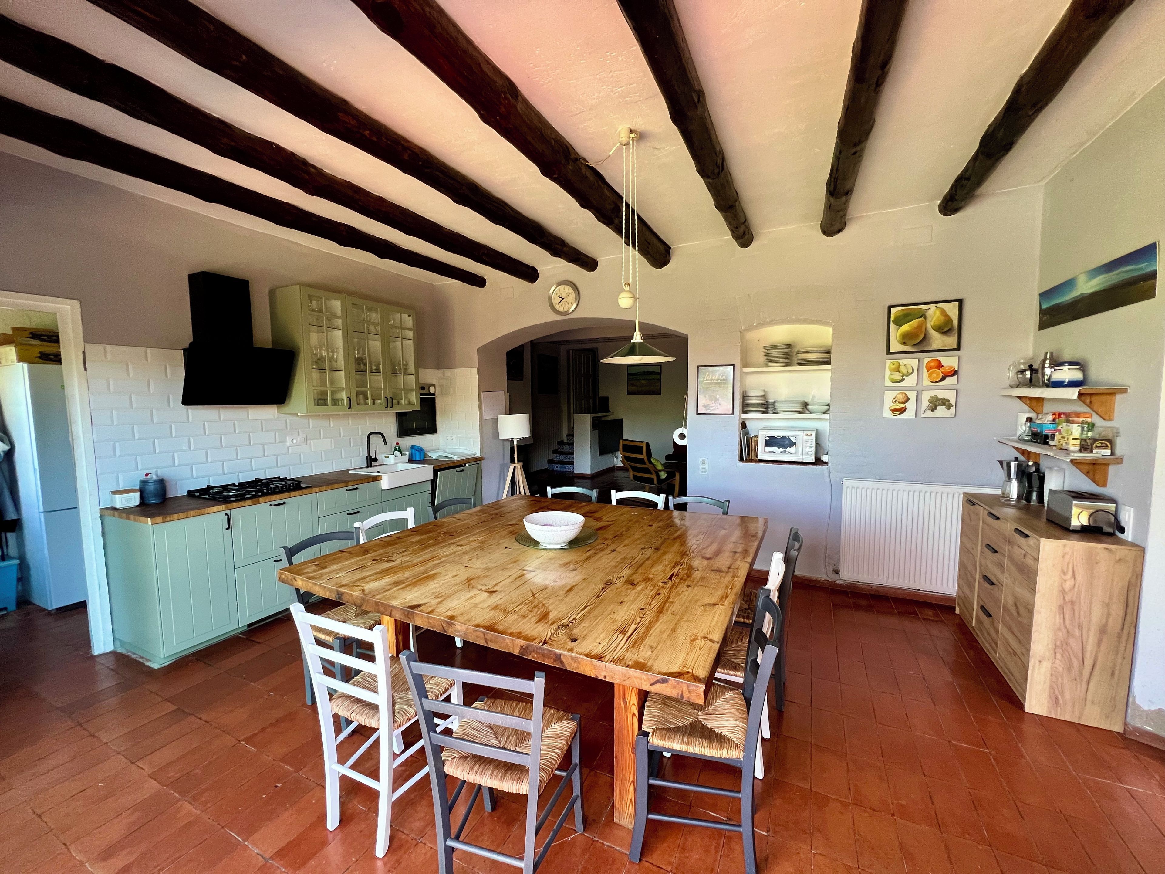 A spacious kitchen with a wooden dining table, white chairs, and a rustic ceiling.