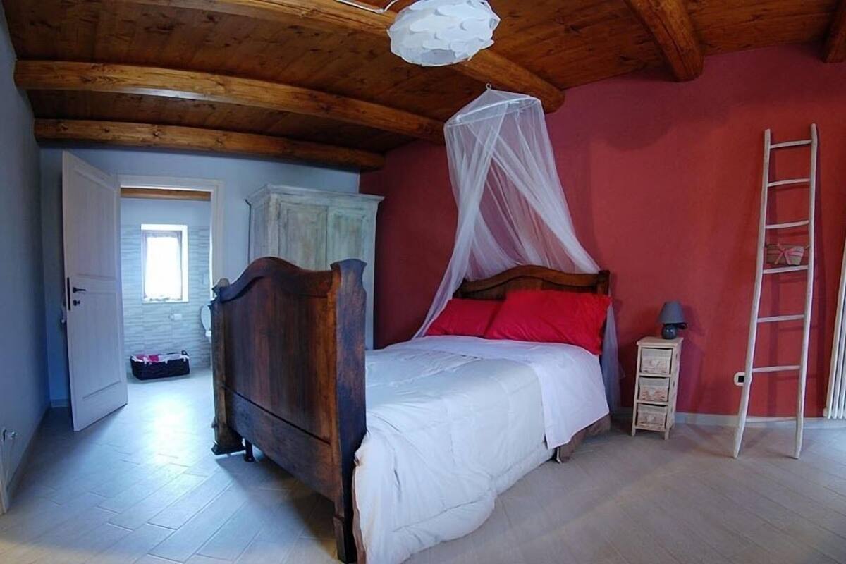 A bedroom with a wooden bed, a white canopy, a red pillow, a nightstand, and a ladder against the wall.