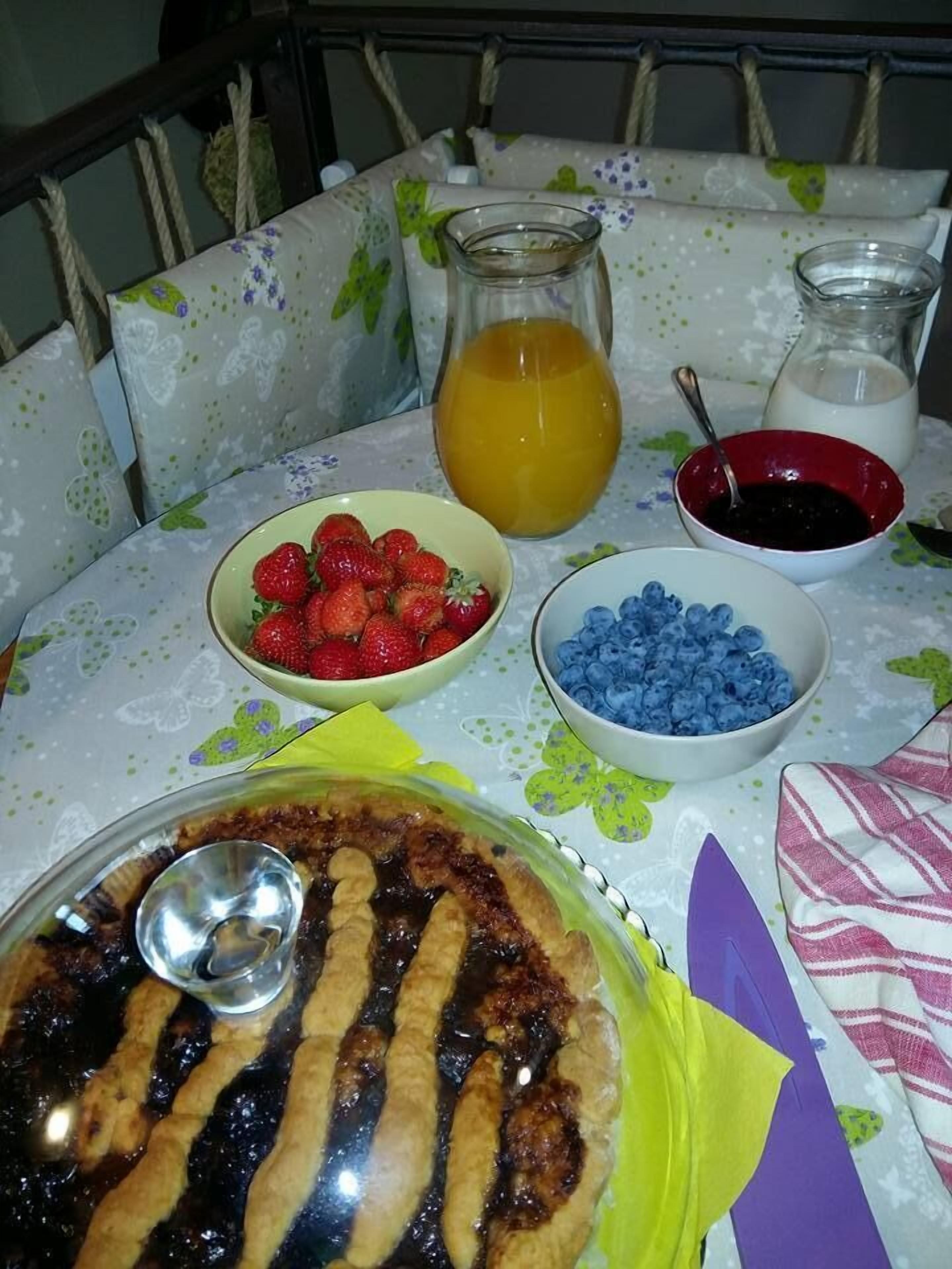 Una tavola imbandita con una crostata, ciotole di fragole e mirtilli, una brocca di succo d'arancia e un boccale di latte.