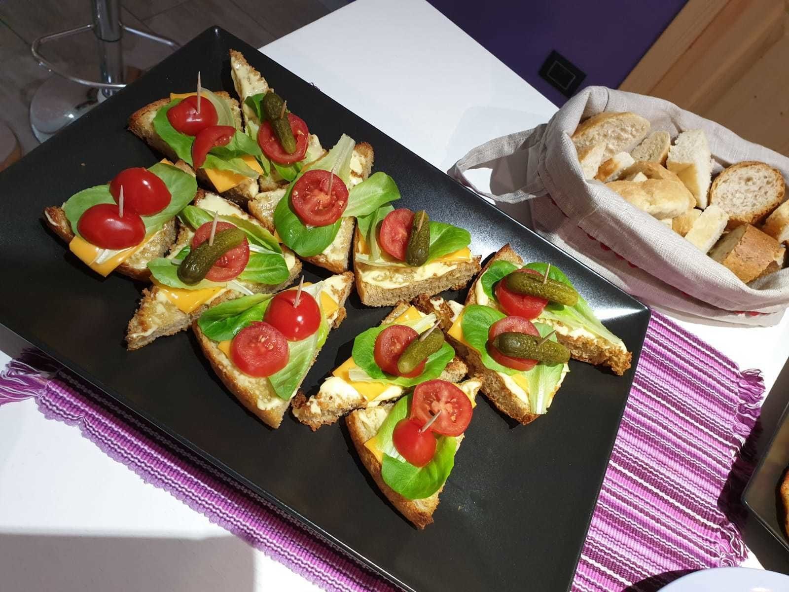 A tray of appetizers with bread, cheese, and tomatoes, and a basket of breadsticks on a table.