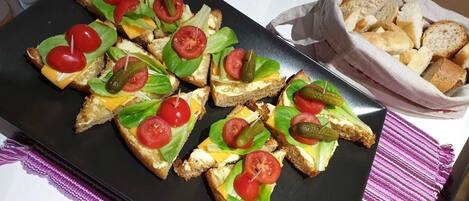 A tray of appetizers with bread, cheese, and tomatoes, and a basket of breadsticks on a table.