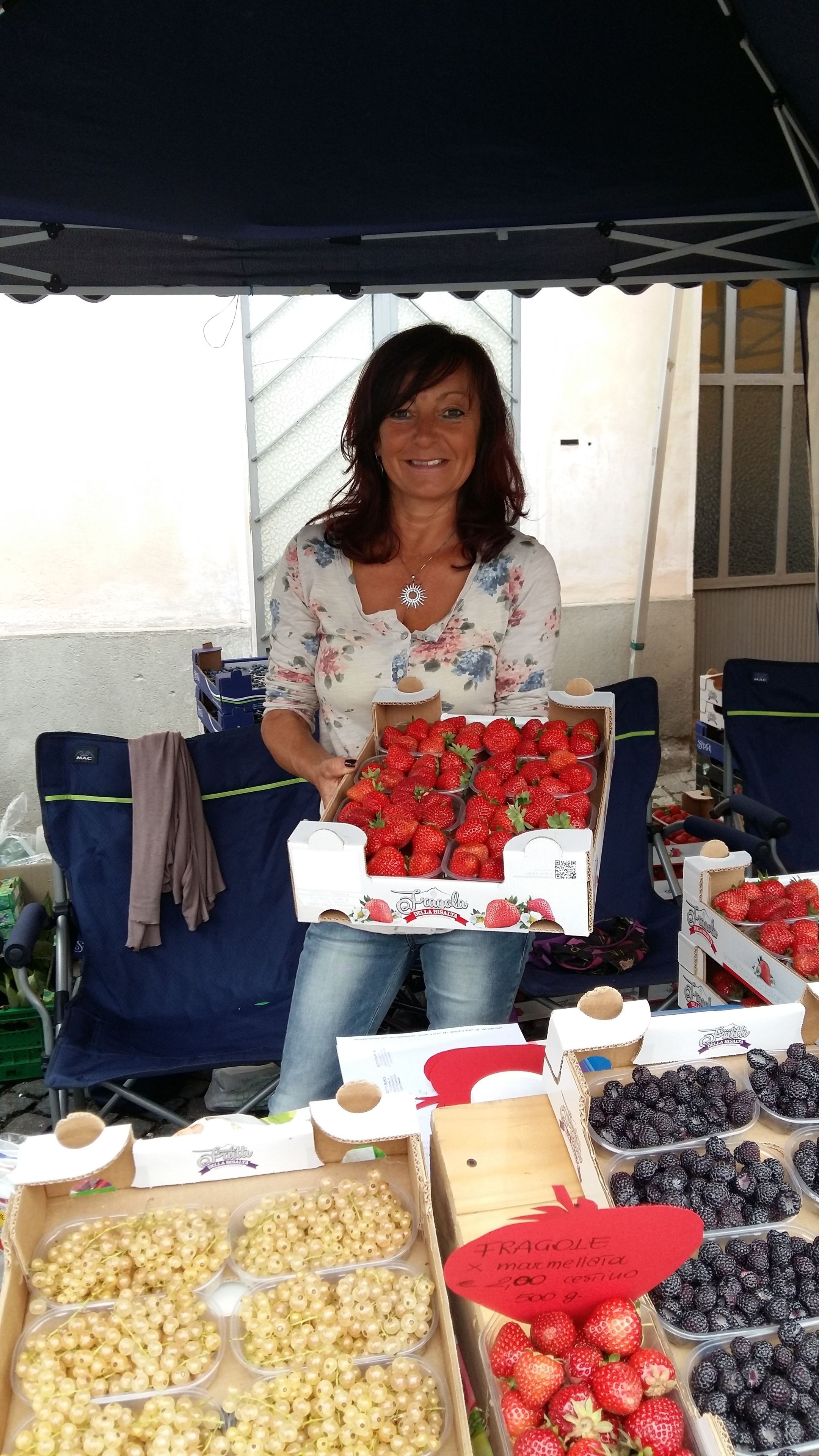 Una mujer de pie detrás de un puesto de frutas con cajas de fresas y frambuesas.
