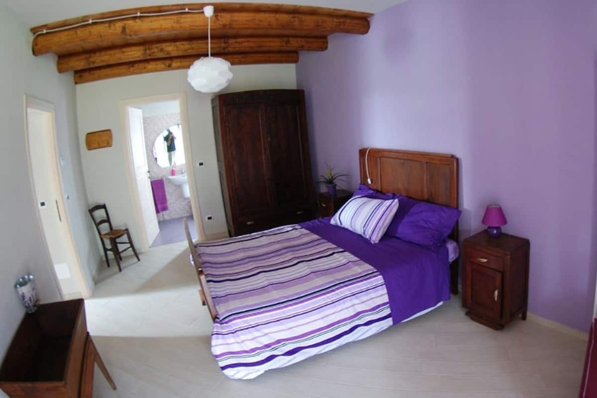 A bedroom with a bed, wooden headboard, bedside table, and a window with blinds.