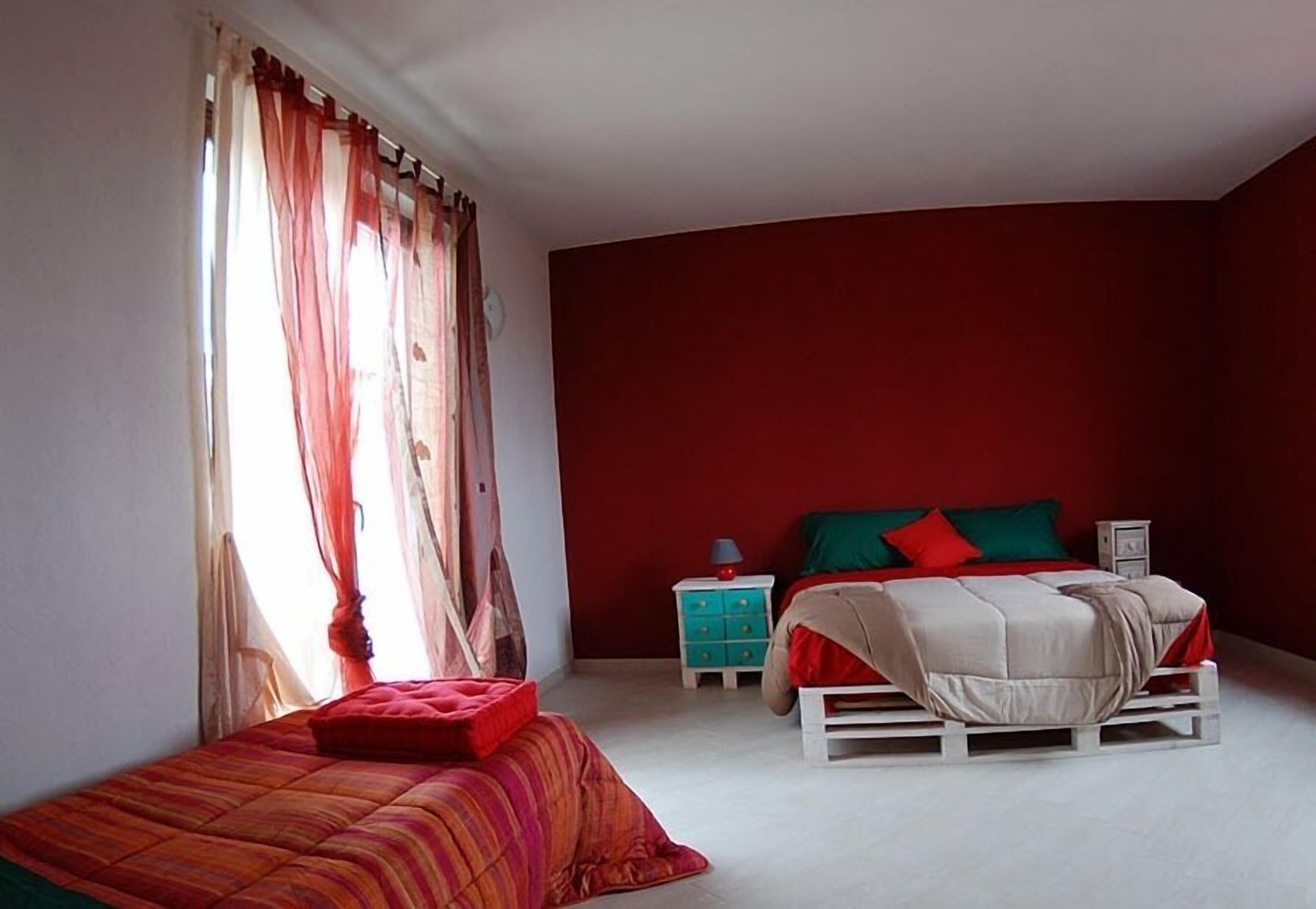 A bedroom with a bed, a nightstand, and a window with sheer curtains.