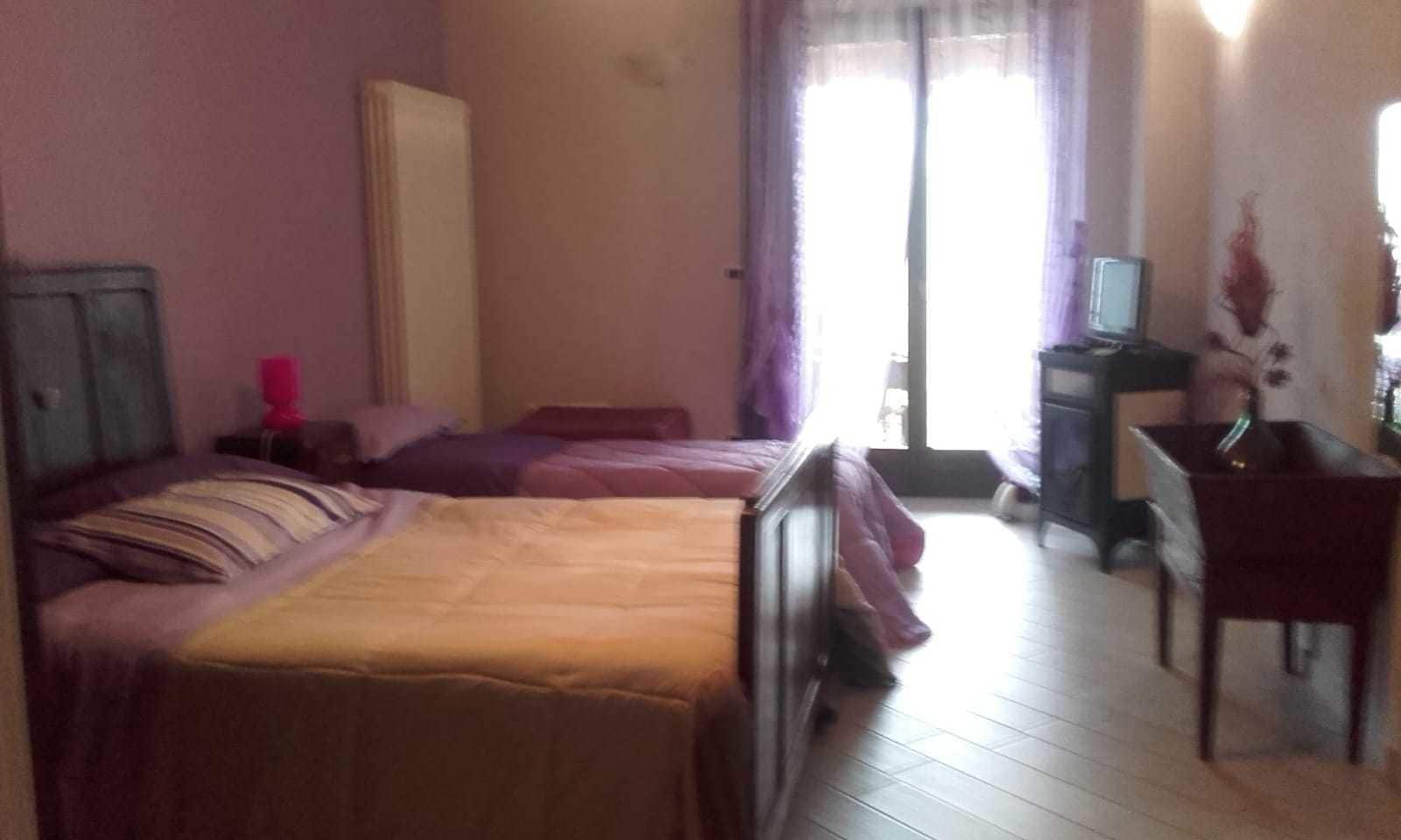 A hotel room with two beds, a desk, a chair, a television, and a window with curtains.