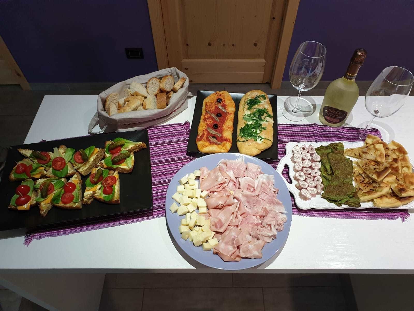 Ein Tisch mit verschiedenen Speisen, darunter Brot, Käse und Fleisch, sowie zwei Weingläser.