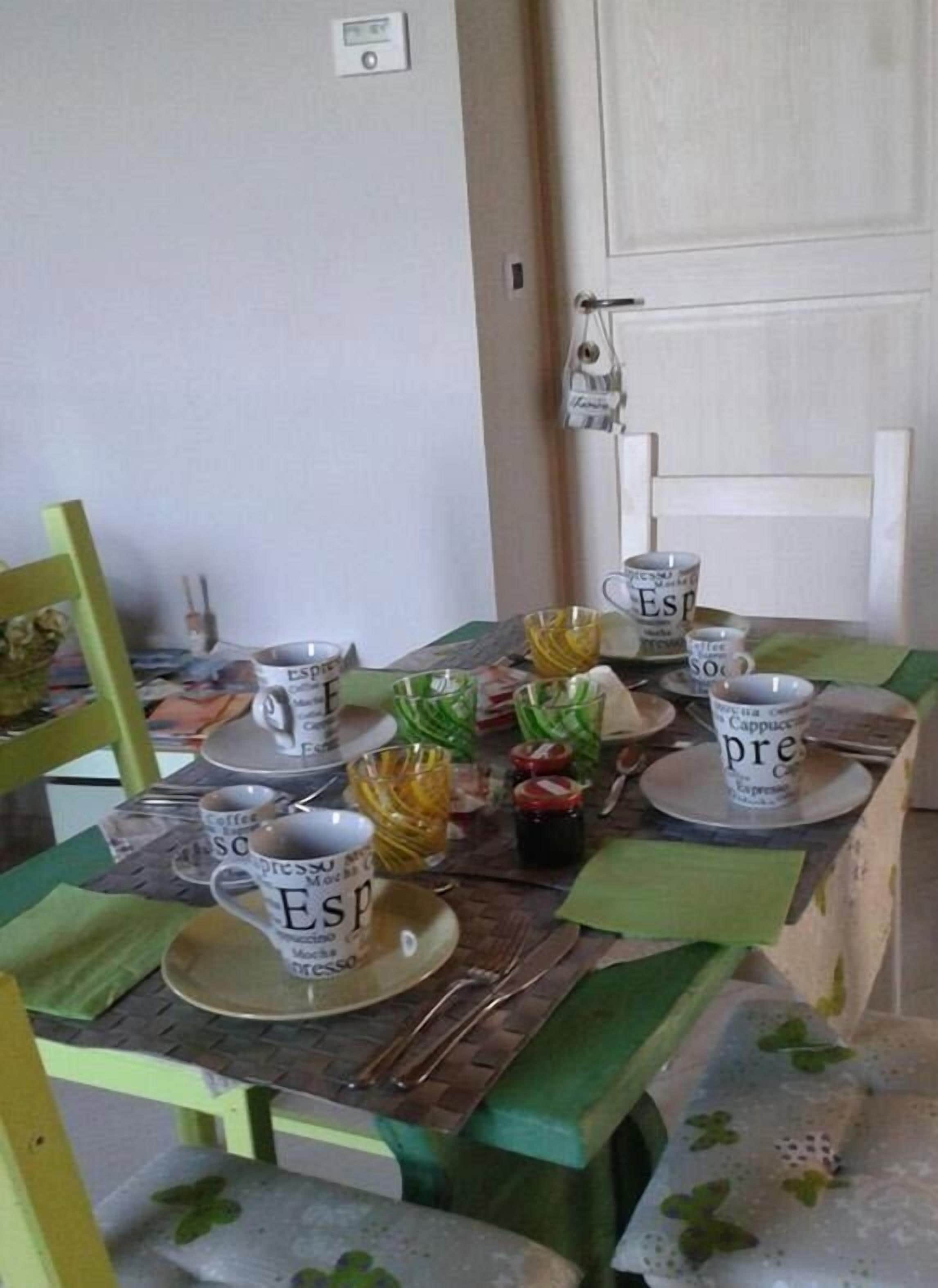 Una mesa de comedor con varias tazas de café y un frasco pequeño de mermelada.