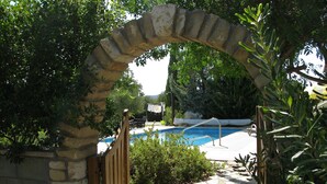Uma área de piscina ao ar livre com entrada em arco de pedra, rodeada por vegetação e um caminho de pedra.