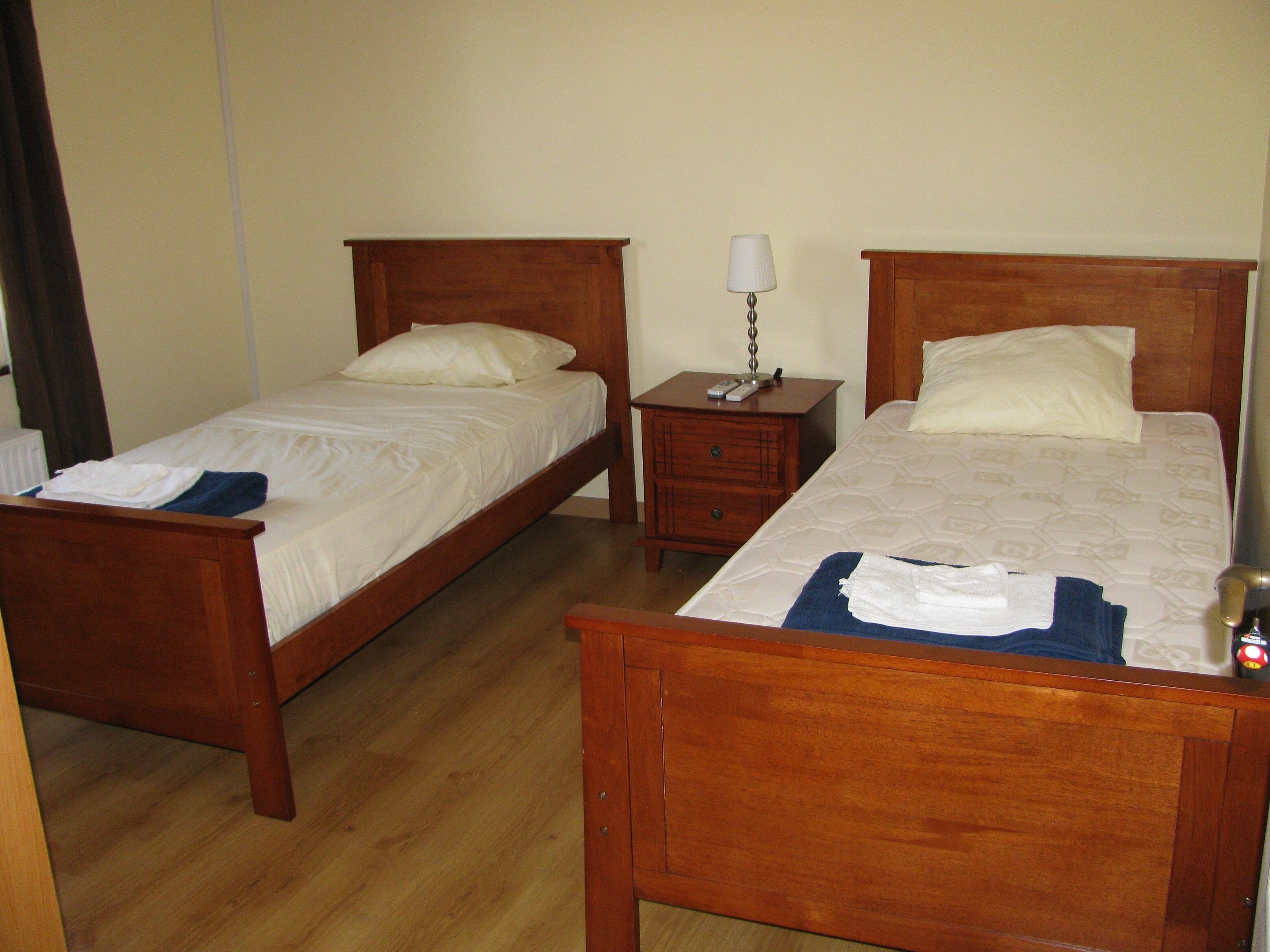 A room with two wooden beds, a nightstand with a lamp, and a radiator.