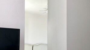 A bedroom with a bed, a TV on a white dresser, and a ceiling fan.