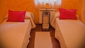 Habitación con dos camas, cada una con un cojín rojo, una mesita con lámpara y suelo de baldosas.