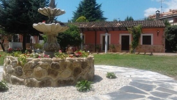 Una fuente de piedra rodeada de flores en un patio con un edificio de techo a tejas al fondo.