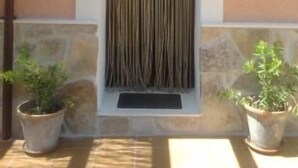 Fachada de edificio con ventanal con persianas verticales, base de piedra y dos macetas a cada lado.