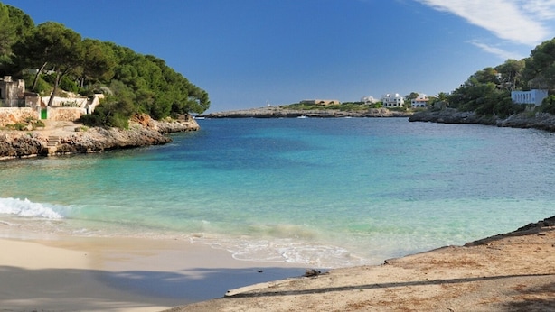 Eine Küstenlandschaft mit klarem türkisblauem Wasser, Sandstrand und Gebäuden entlang der Uferlinie.