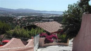 A residential area with a house featuring a tiled roof, surrounded by greenery and a clear view of a distant town. - Apartment in villa, sea view from bedrooms (Hyères)