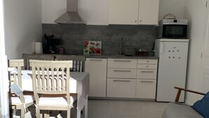 A compact kitchen with white cabinets, a microwave, and a refrigerator. There is a dining area with a table and chairs. - Apartment in villa, sea view from bedrooms (Hyères)