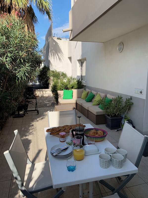 An outdoor patio with a table set for breakfast, including bread, pastries, and beverages. - Two bedroom apartment near to charming historic port (Marseillan)