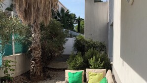 Un espace extérieur ensoleillé, aménagé avec un canapé, des coussins et une bouteille de champagne posée sur un plateau.