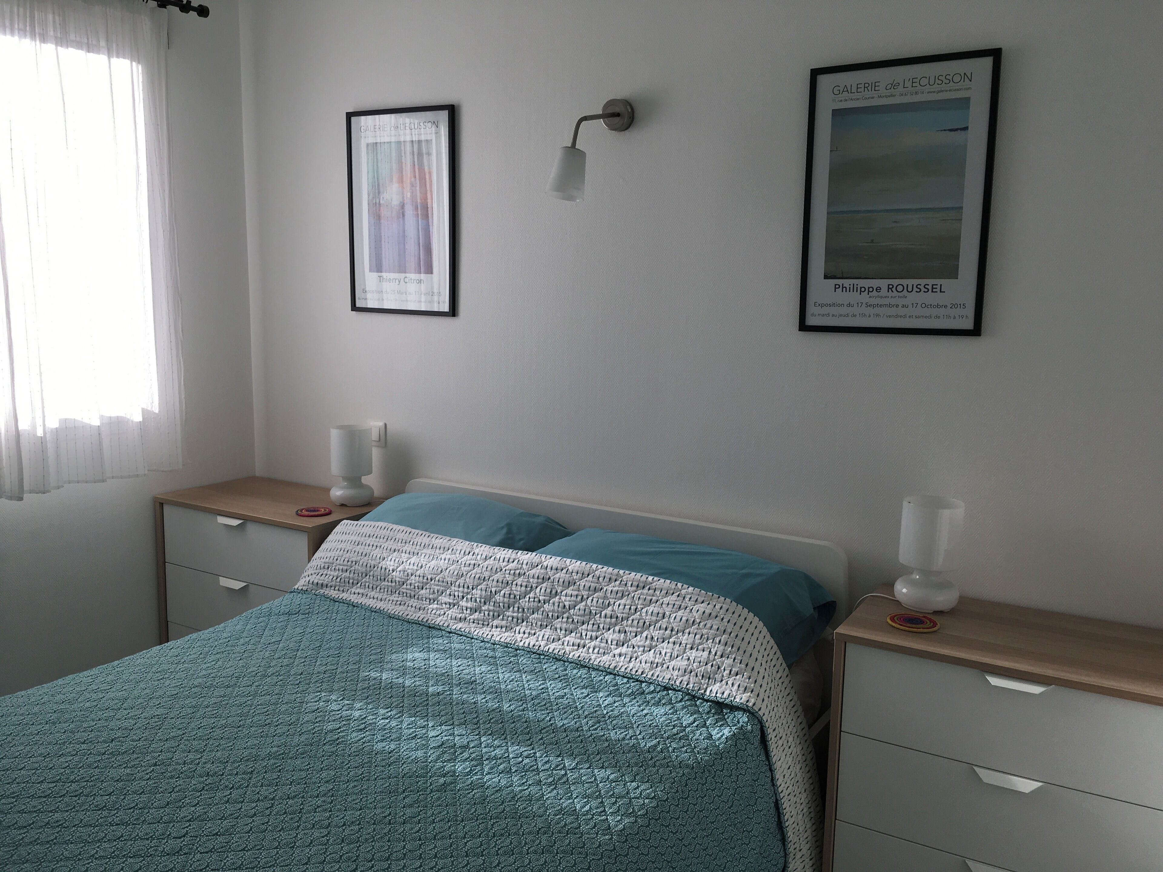 A bedroom with a bed, bedside tables, a lamp, and two framed artworks on the wall.