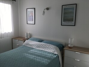 A bedroom with a bed, bedside tables, a lamp, and two framed pictures on the wall. - Two bedroom apartment near to charming historic port (Marseillan)