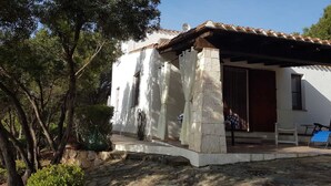 A white building with a tiled roof, a stone entrance, and a covered porch area. - Villa "The lapwing one" (semi-detached portion of the sea) (Marina di Tertenia, Tertenia (OG))
