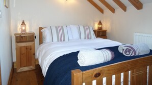 A bedroom with a wooden bed frame, white bedding, striped pillows, a blue blanket, and two bedside lamps. - Character 2 bedroom barn conversion in peaceful rural setting (Norwich)