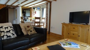 A living room with a black leather sofa, a wooden coffee table, and a television on a wooden cabinet. - Character 2 bedroom barn conversion in peaceful rural setting (Norwich)