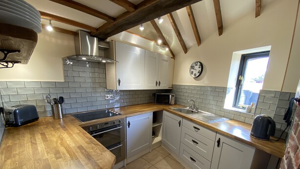 A kitchen with a wooden countertop, stainless steel appliances, white cabinets, and a tiled backsplash. - Character 2 bedroom barn conversion in peaceful rural setting (Norwich)