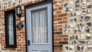 A building with a stone facade, a grey door, and a small sign reading "Partridge Barn". - Character 2 bedroom barn conversion in peaceful rural setting (Norwich)