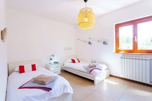 A bedroom with two beds, a window, a radiator, and a hanging light fixture.