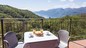 Een ontbijt staat gedekt aan een tafel op een balkon met uitzicht op een bergachtig landschap.