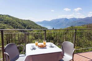 Ein Tisch ist mit Frühstück auf einem Balkon gedeckt, mit Blick auf eine gebirgige Landschaft.