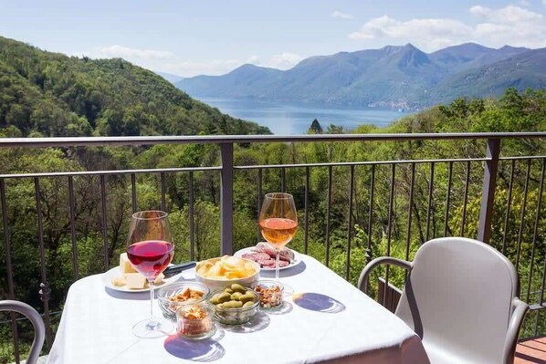 Ein Tisch im Freien mit Blick auf Berge und See, gedeckt mit Weingläsern, Käse, Oliven und Nüssen.