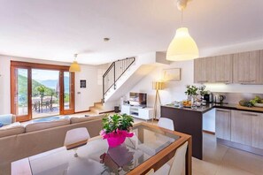 A modern living room with a glass dining table, a sofa, and a staircase leading to an upper floor. - Stunning Italian Lakes villa with lake views (Dumenza)