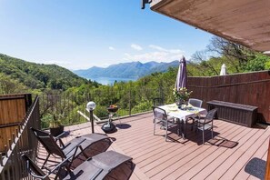 Eine Holzterrasse mit Tisch und Stühlen, mit Blick auf eine Berglandschaft und ein Gewässer.