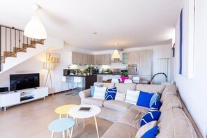 A modern living room with a sofa, coffee table, and TV, connected to a kitchen with a dining area and staircase. - Stunning Italian Lakes villa with lake views (Dumenza)