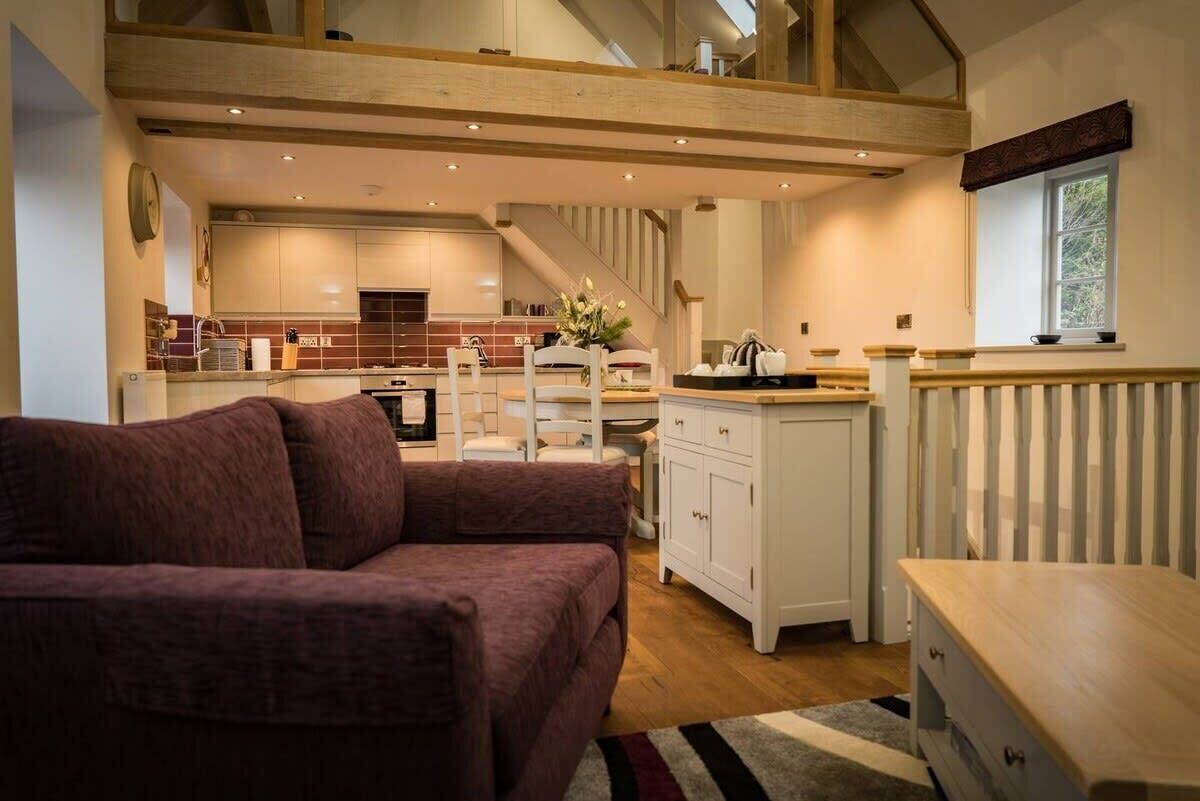 A cozy living area with a sofa, a wooden dining table, and a kitchen in the background.