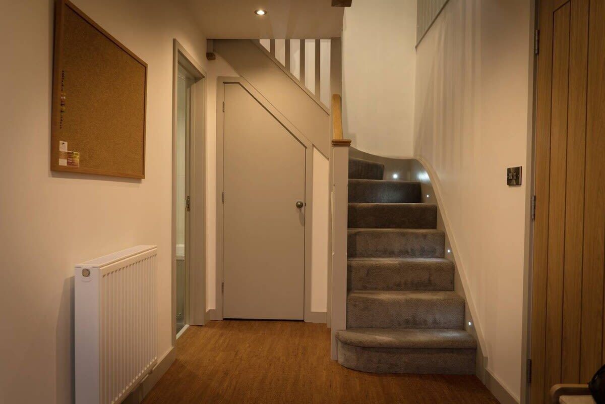 Un couloir avec un escalier recouvert de moquette, un radiateur et une porte donnant sur une autre pièce.