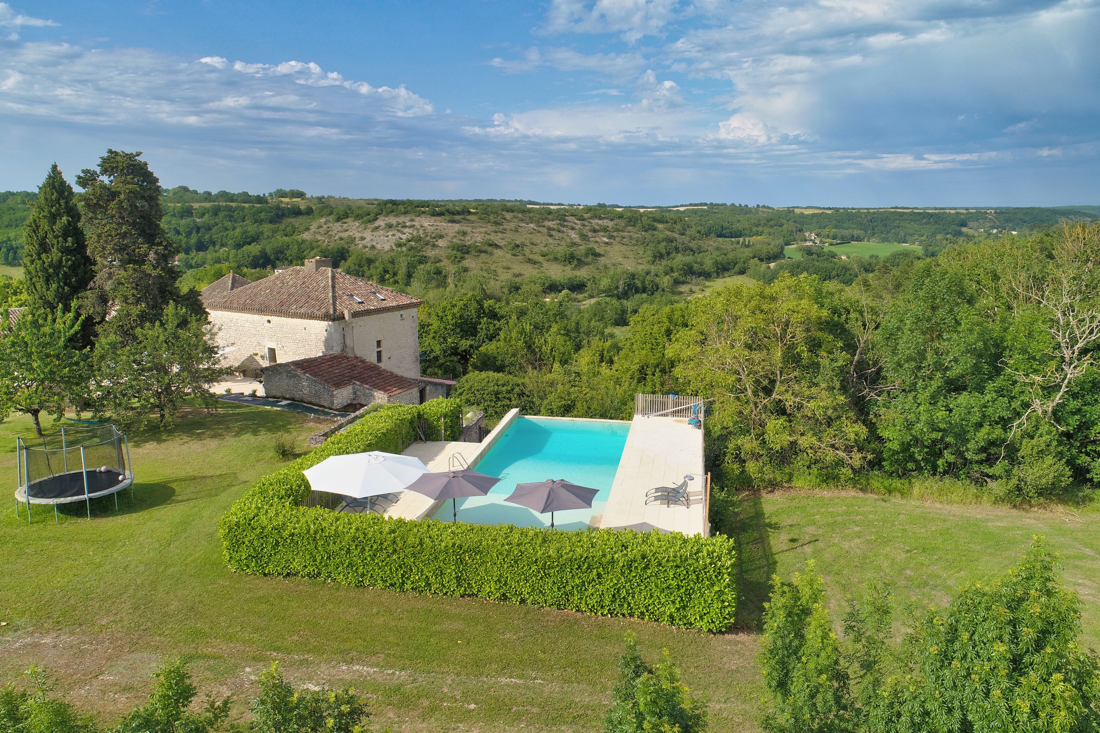 A house with a swimming pool, surrounded by lush greenery and a clear sky.
