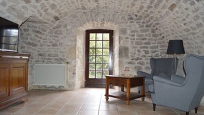 Habitació amb sostre de pedra, un armari de fusta, una butaca blava, taula de fusta petita i finestra amb vista a arbres.