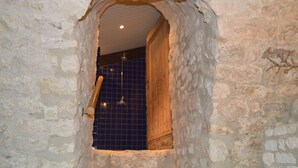 Habitació amb parets de pedra, una porta de fusta i un mur revestit de rajoles.