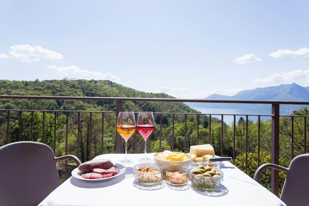 Mesa preparada con comida y bebidas en un balcón con vistas a un paisaje montañoso.