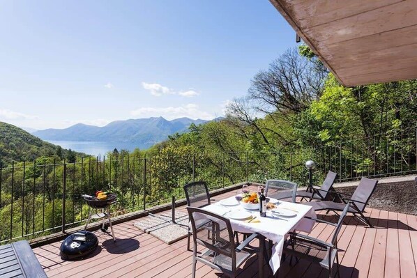 An outdoor dining area with a table set for two, surrounded by chairs, overlooking a scenic view of mountains and a lake. - Family friendly Italian Lakes villa rental (Dumenza)