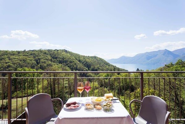 Une table dressée à l’extérieur, offrant une vue imprenable sur les montagnes, avec deux verres de vin et divers plats.