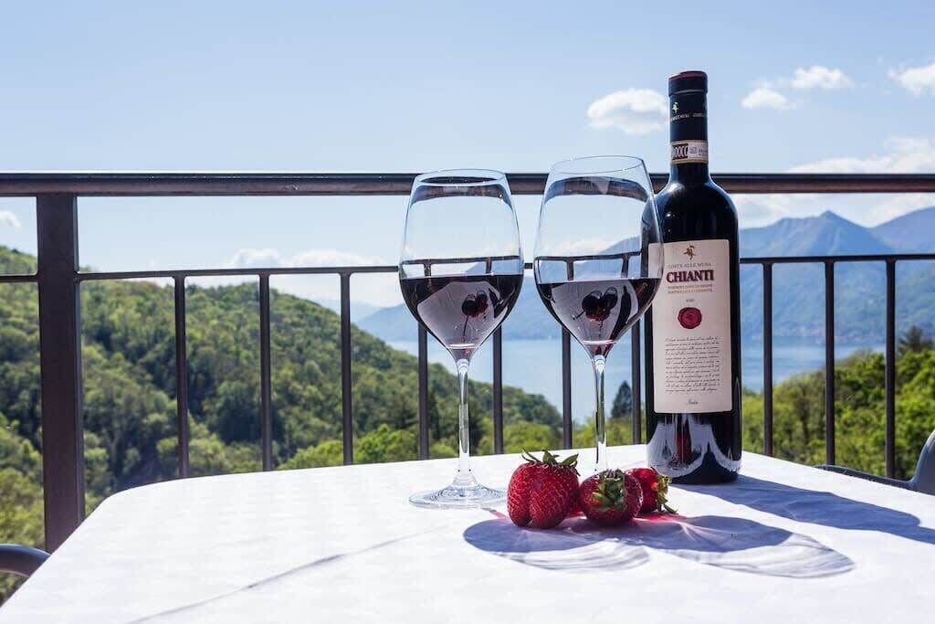 A table with two wine glasses and a bottle of Chianti wine, set against a scenic mountain backdrop.
