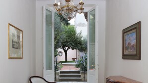 Un corridoio con un lampadario, una porta che dà all'esterno e un piccolo tavolo con un libro.