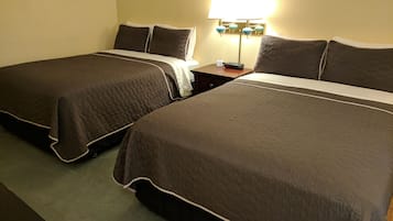 A hotel room with two queen-sized beds, a nightstand with a lamp, and a wall clock.