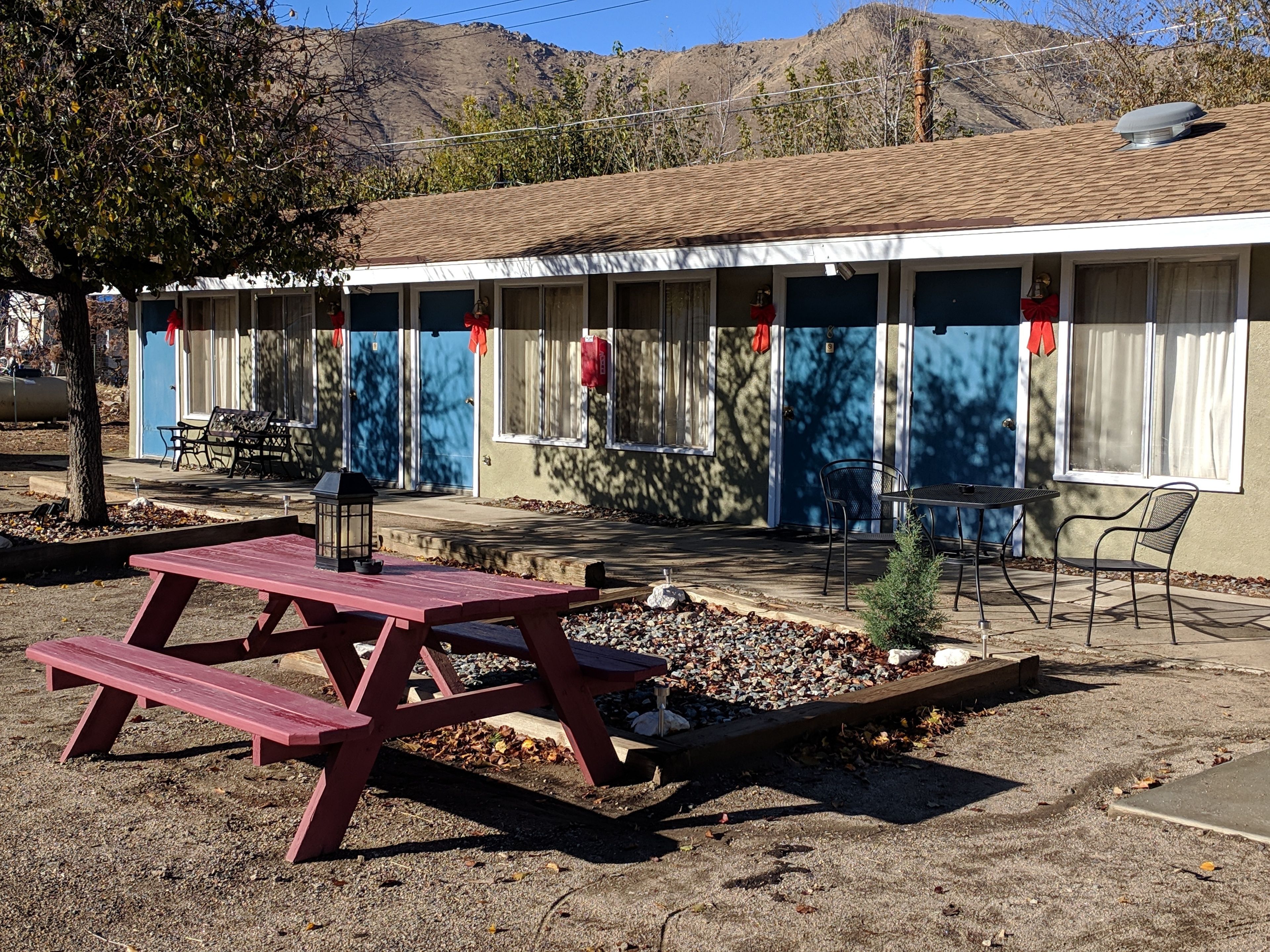 A motel with a covered outdoor seating area, a picnic table, and a small garden.