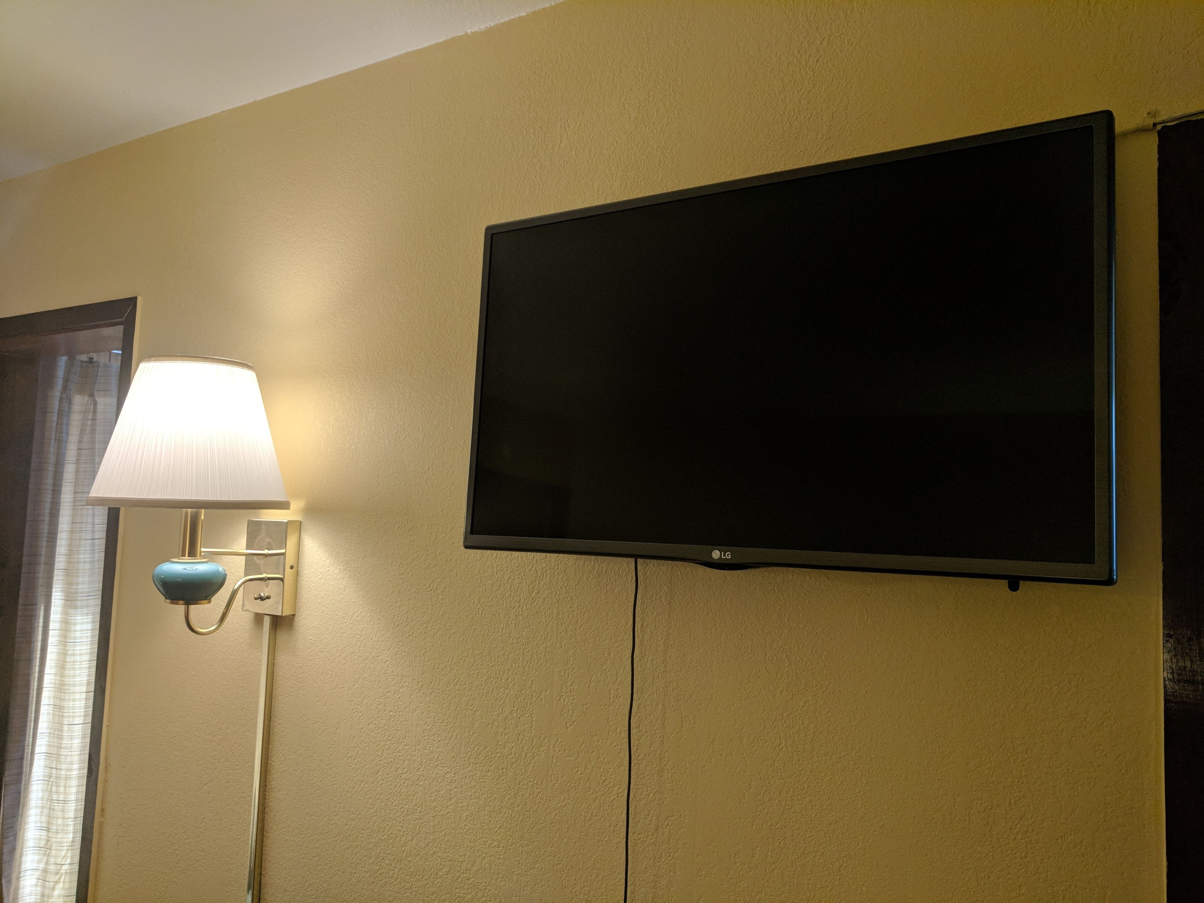 Un televisor de pantalla plana montado en la pared y una lámpara también fijada a la pared en una habitación con paredes color beige.
